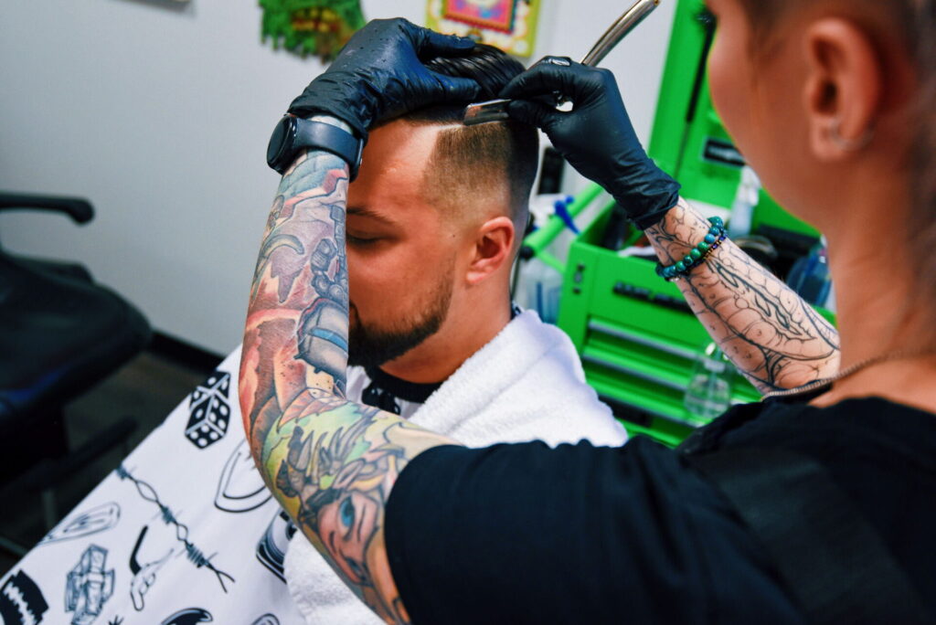 Tattooed barber giving man a haircut.