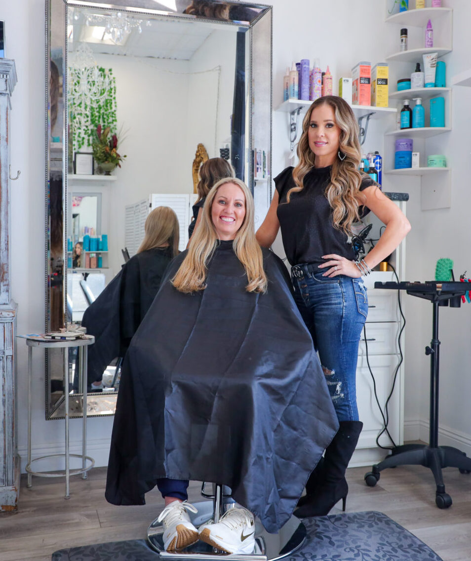 Hairdresser with client at salon, mirror reflection visible.