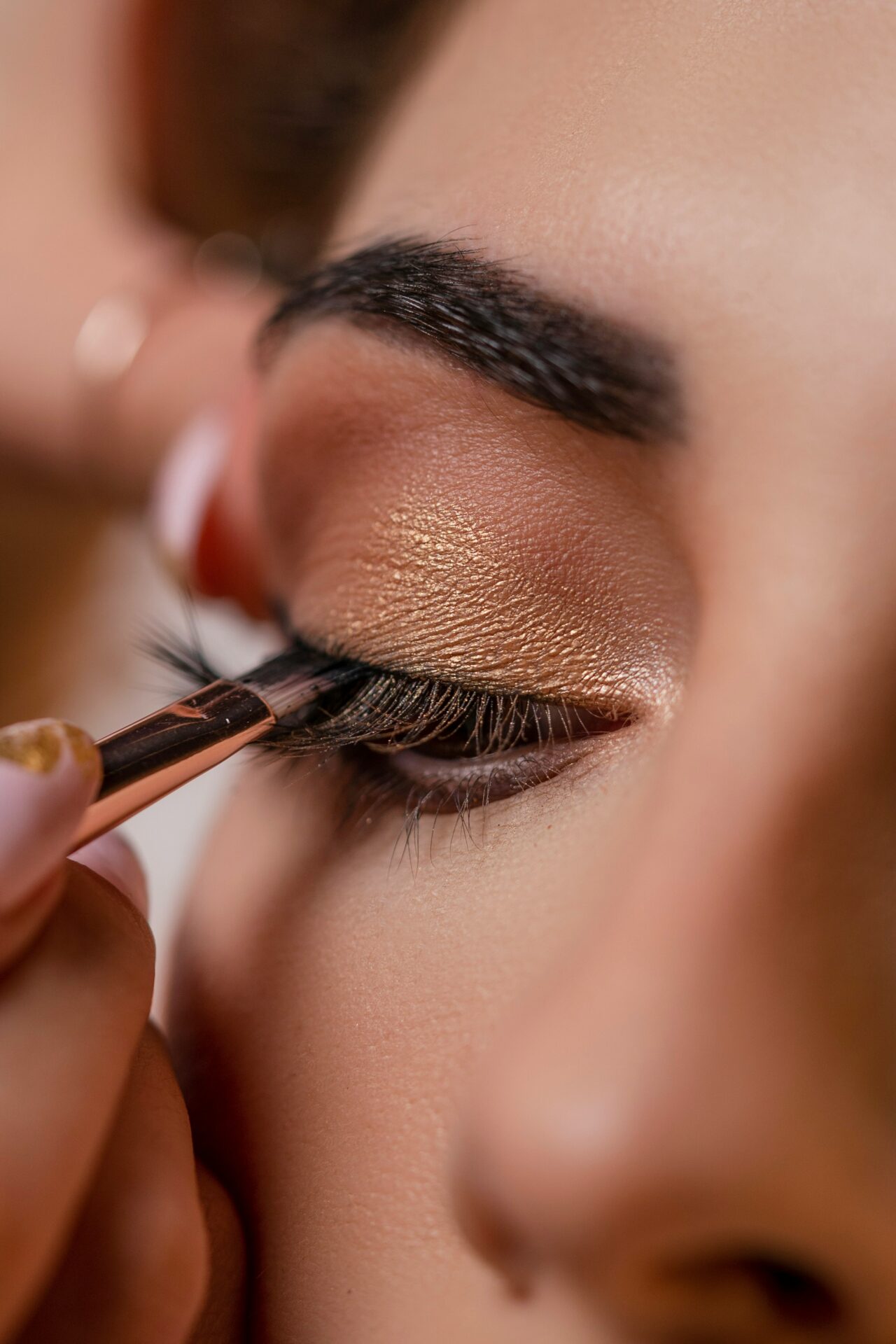 Applying gold eyeshadow with brush, close-up view.